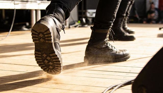 Stomping leather boots kicking dust on sunlit wooden stage during live performance