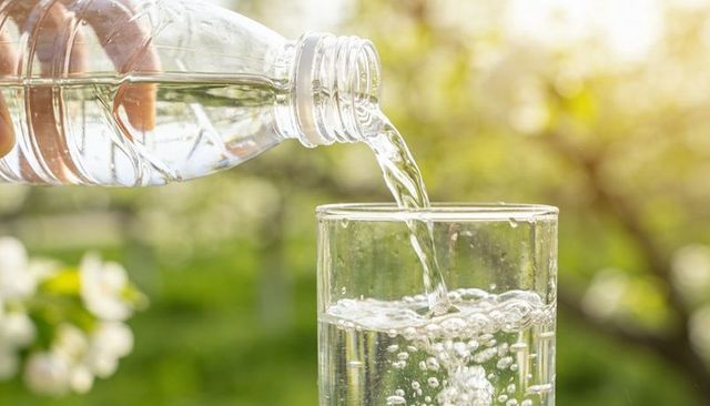 Pouring clear water from plastic bottle into glass with bubbles and sunlit garden bokeh