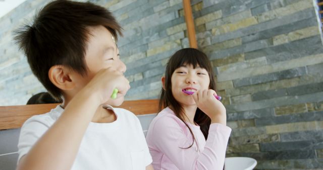 Two children are smiling and brushing their teeth together in a modern bathroom, promoting good dental habits. Ideal for articles on parenting, dental care routines, healthy habits for children, or family dynamics. This image can be used for marketing dental products designed for kids, educational material on oral hygiene, or family well-being advertisements.