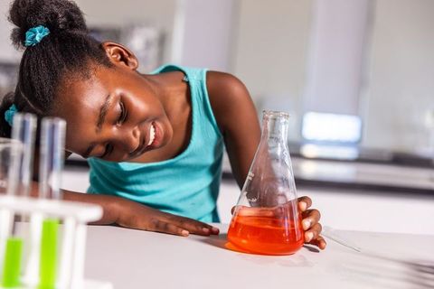 African-american girl exploring colorful chemistry with orange flask in school lab