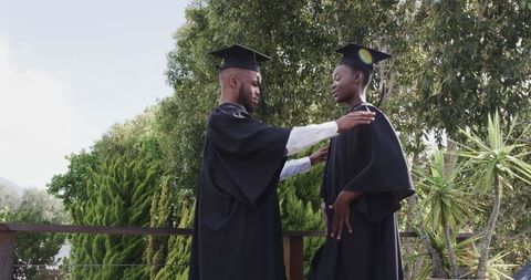 Graduating friends adjusting caps celebrating academic success outdoors