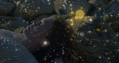 Serene woman dreaming amid glowing particles in cozy bedroom