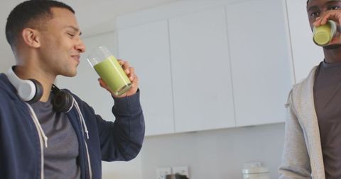 Diverse friends enjoying green smoothies in modern kitchen wearing hoodies, healthy lifestyle
