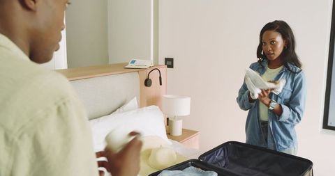 Friends packing suitcase in stylish bedroom holding sneaker and mug
