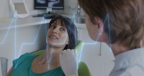 Dentist examining patient in dental chair with ecg overlay and x-ray monitor, modern clinic