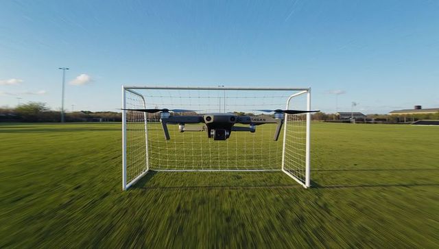 Hovering drone filming inside soccer goal on sunlit sports field with dynamic perspective