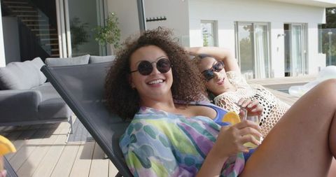 African american women lounging poolside wearing sunglasses sipping lemon cocktails by modern deck