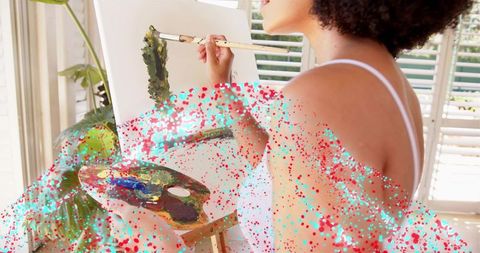 Female artist painting on canvas at sunlit easel with palette and long brush