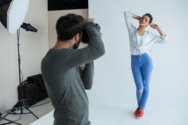 Female model posing confidently for a photographer in a professional studio. She is wearing a casual outfit with blue jeans and red shoes, striking a stylish pose. This image is ideal for use in fashion magazines, photography tutorials, modeling portfolios, and creative industry advertisements.