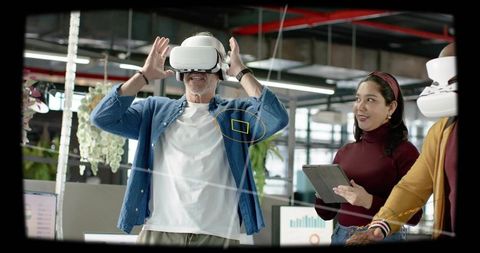 Mature man testing vr headset in modern open-plan office with colleague holding tablet