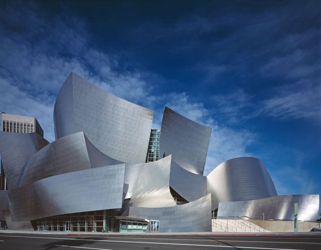 Showcasing the stunning exterior of the Walt Disney Concert Hall in Los Angeles, this image highlights its unique, modern architectural design created by Frank Gehry. With dynamic shapes and reflective metal surfaces under a bright blue sky, this photo provides a striking visual of this iconic cultural landmark. Ideal for use in content related to architecture, travel, and cultural landmarks.