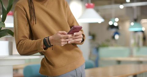 Man Leaning on Counter Tapping Smartphone in Cozy Coworking Space with Minimalist Design