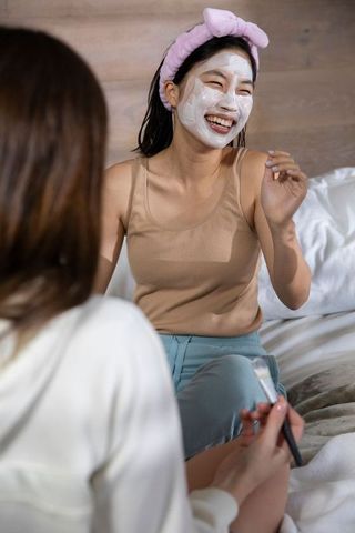 Asian Friends Laughing and Applying Facial Masks in Bed