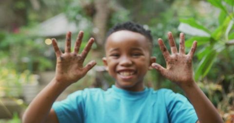 Smiling african american child showing muddy hands in backyard garden, joyful outdoor play