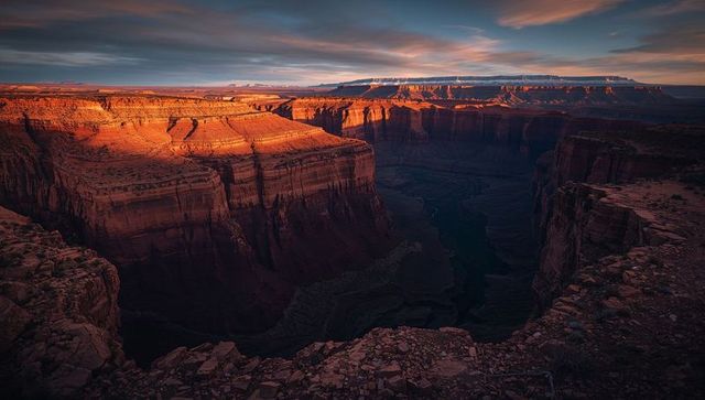 Glowing sunset lighting dramatic layered sandstone canyon overlooking winding river gorge