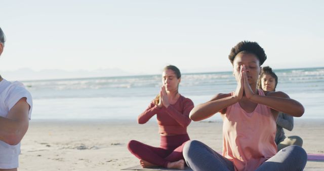 People meditating on the beach during sunrise. Diverse group practicing mindfulness and wellness in natural outdoor environment. Suitable for illustrating concepts of serenity, mental health, wellness retreats, yoga classes, and group activities.