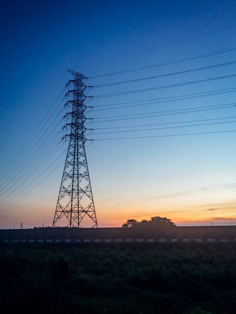 Power tower with electric lines framed by a stunning sunset sky, showcasing infrastructure against a natural evening backdrop. Ideal for use in energy and power supply-related content, environmental studies illustrating industry and nature, or promotional materials for utilities and communication companies.