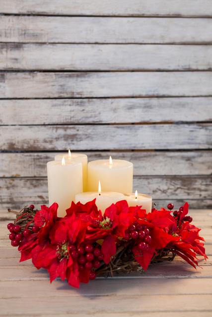 Christmas candles adorned with a poinsettia and berry wreath on a rustic wooden background. Ideal for holiday greeting cards, festive home decor inspiration, seasonal blog posts, and Christmas-themed advertisements.