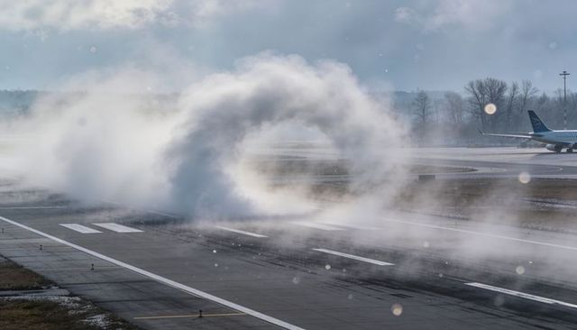 Circular vapor vortex forming over runway during cold winter airport operations with jet tail