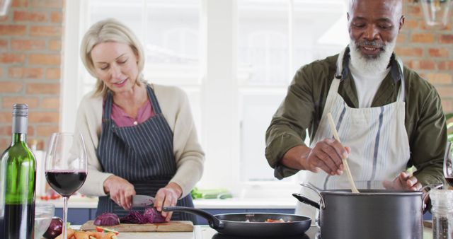 Biracial senior couple wearing aprons cooking together in the kitchen at home. retirement senior couple lifestyle living concept