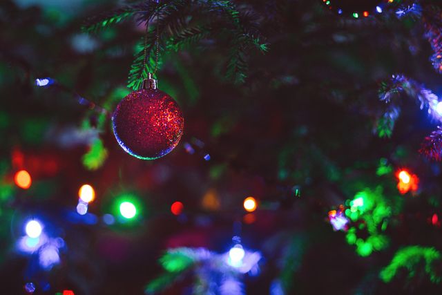 Close-up of a Christmas tree with a red ornament and vibrant, colorful lights in the background. Perfect for holiday greeting cards, festive advertisements, seasonal social media posts, and holiday-themed blog articles.
