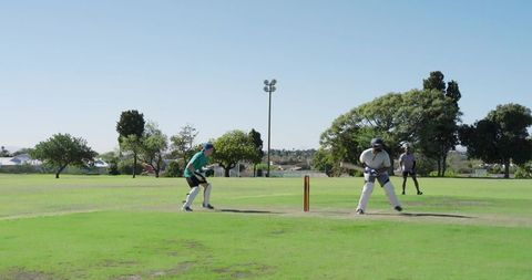 Community cricket match in sunny park with batsman preparing shot and wicketkeeper ready