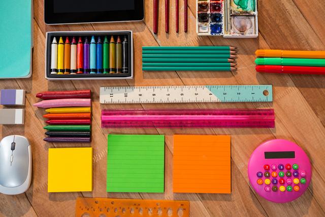 Colorful stationery items including pencils, crayons, rulers, sticky notes, and a calculator are neatly arranged on a wooden table. Ideal for use in educational materials, back-to-school promotions, office supply advertisements, and creative project inspirations.