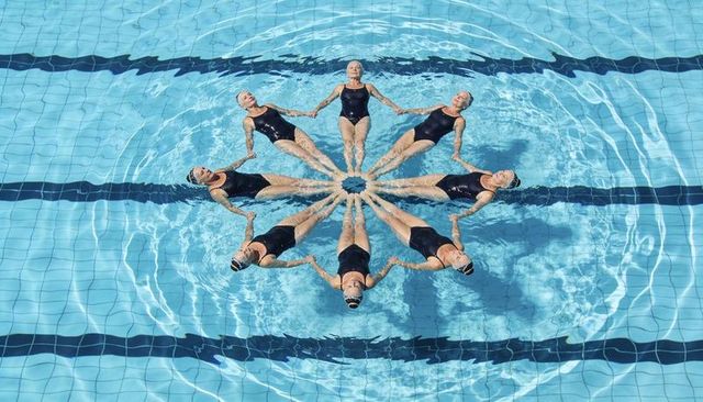 Eight synchronized swimmers forming star formation while floating on backs in pool