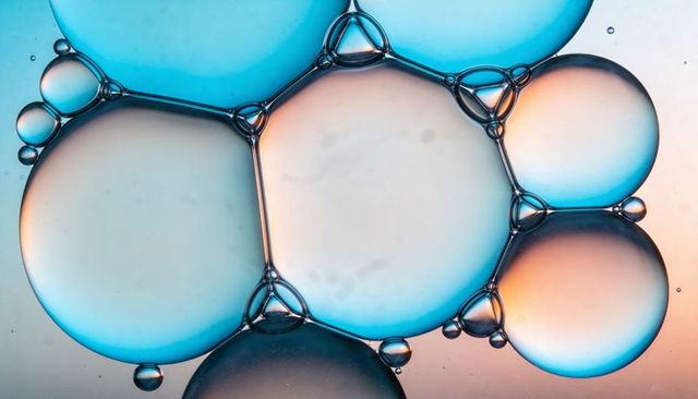 Glistening macro oil bubbles forming geometric cluster with blue and warm gradient light
