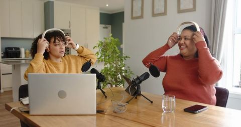 Recording lively home podcast with friends putting on headphones at kitchen table cohosts
