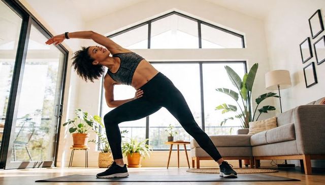 Woman stretching in sunlit living room practicing yoga and home workout with plants
