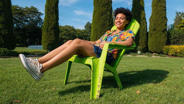 Smiling woman reclining in lime-green lawn chair on sunny manicured garden lawn