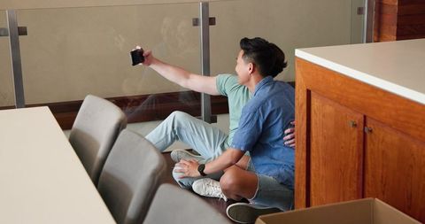 Diverse Male Couple Sitting on Floor Taking Selfie at Home