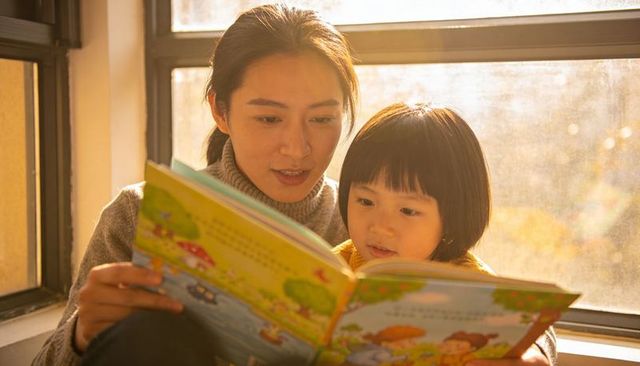 Woman and child reading together on sunlit window seat, cozy backlit family storytime