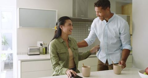 Asian couple enjoying morning coffee at modern kitchen island, smiling and chatting