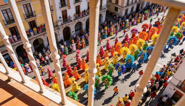 Balcony view of rainbow carnival parade with feathered dancers in flowing colorful gowns