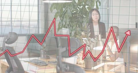 Office team analyzing rising red chart overlay on modern open-plan workspace monitors