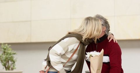 Middle-aged couple sharing kiss in urban plaza with bouquet of white flowers