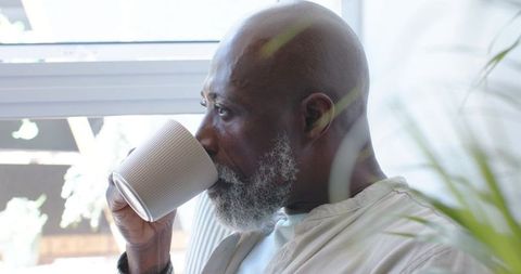Senior african american man sipping coffee by sunlit window relaxing at home quiet morning