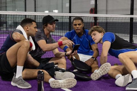 Young diverse male athletes reviewing game strategy on smartphone during padel court break