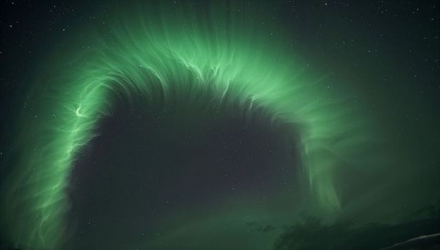 Emerald aurora arch dancing across starry polar sky with wispy curtains and distant horizon
