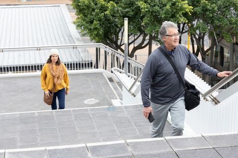 Senior man and woman in beanie climbing urban stairs with railing during overcast city commute