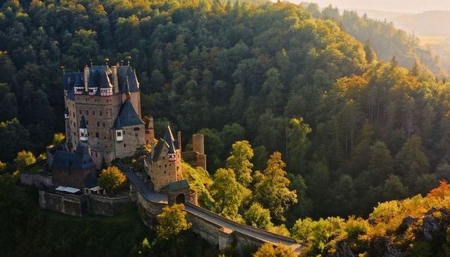 Medieval stone keep perching on forested hilltop, golden hour bridge and causeway