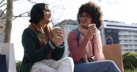 Diverse Friends Sharing Coffee and Laughter on Urban Park Bench After Shopping