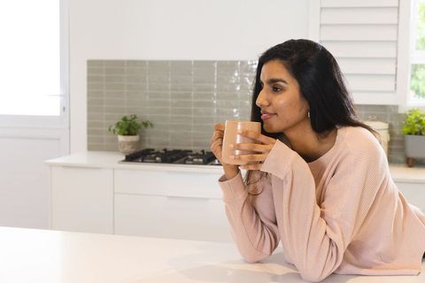 Serene asian woman relaxing in modern kitchen holding mug