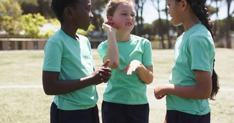 Diverse teen girls chatting and bonding on sunny sports field wearing green shirts