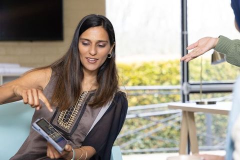 Indian woman pointing at smartphone while collaborating with coworker in office lounge