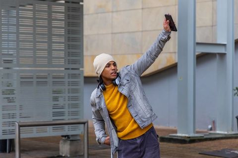 Young man holding phone aloft leaning back and looking up in modern urban plaza