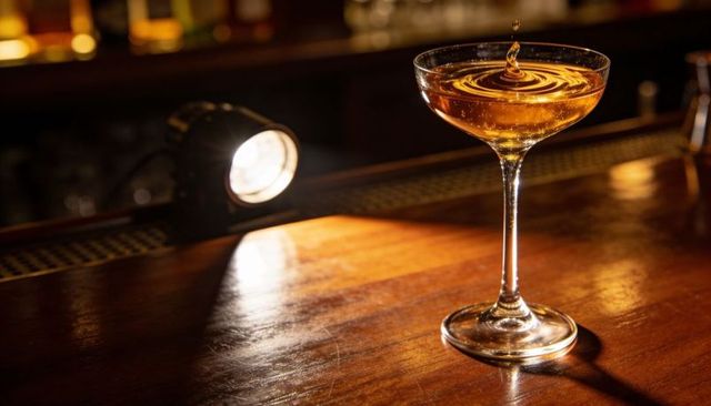 Amber cocktail ripple in coupe glass under spotlight on polished wooden bar
