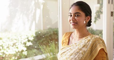 Sunlit indian woman wearing gold saree by starred window, serene jewelry portrait